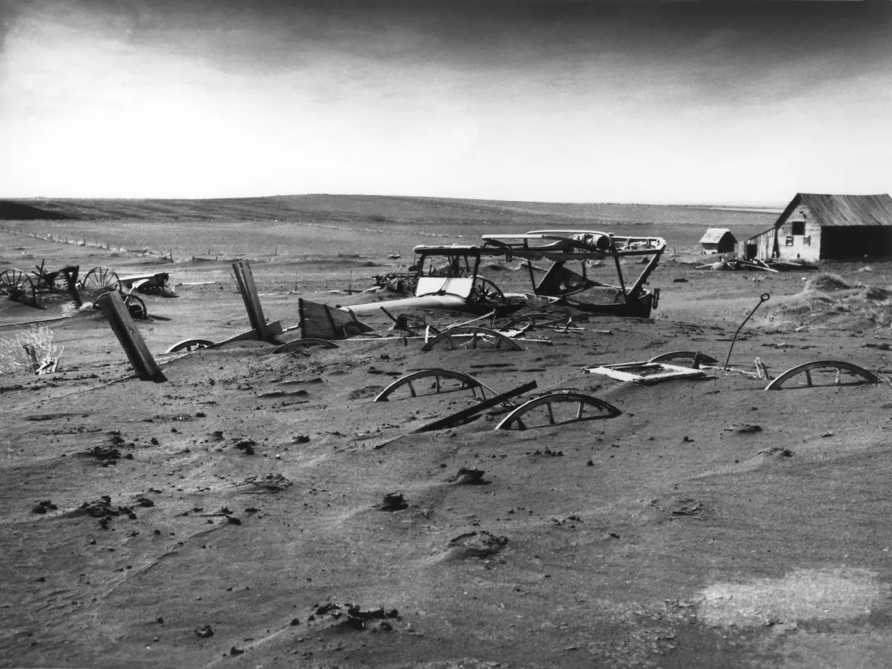 Buried machinery in barn lot in Dallas, South Dakota, United States during the Dust Bowl, an agricultural, ecological, and economic disaster in the Great Plains region of North America in 1936. Sourced from United States Department of Agriculture, Image Number: 00di0971/Wikimedia Commons. Image in the Public Domain.